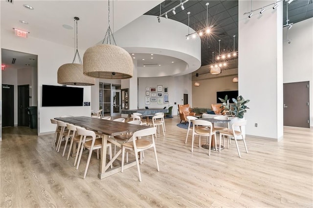 dining area featuring track lighting, light hardwood / wood-style floors, and a high ceiling