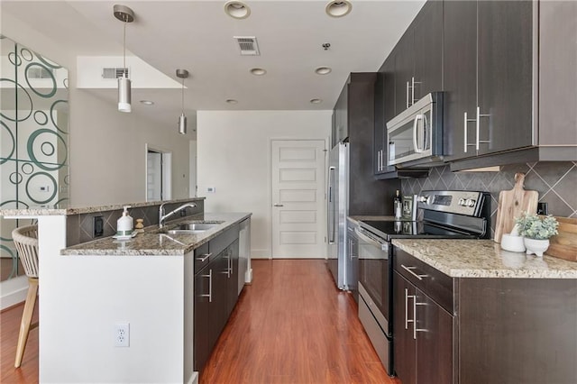 kitchen featuring sink, hardwood / wood-style floors, stainless steel appliances, a kitchen breakfast bar, and decorative light fixtures