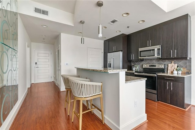 kitchen featuring appliances with stainless steel finishes, a breakfast bar area, hanging light fixtures, a center island, and light hardwood / wood-style flooring