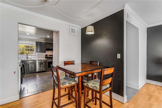 dining space with crown molding, light hardwood / wood-style floors, and sink