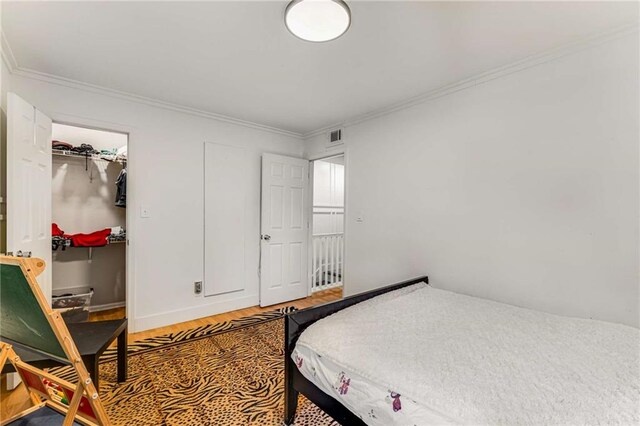 bedroom featuring ornamental molding, hardwood / wood-style floors, a walk in closet, and a closet