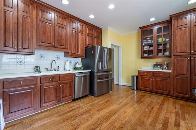 kitchen with a sink, backsplash, light wood-style floors, appliances with stainless steel finishes, and light countertops