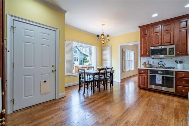 kitchen featuring crown molding, light wood-type flooring, a chandelier, and stainless steel appliances