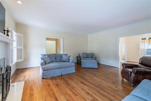 living area with a high end fireplace, crown molding, baseboards, light wood-style floors, and an inviting chandelier