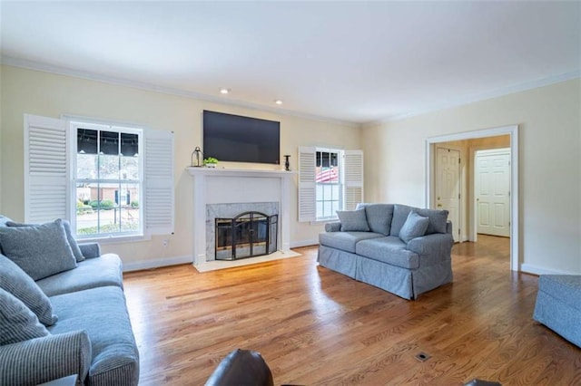 living room with a premium fireplace, wood finished floors, baseboards, and ornamental molding