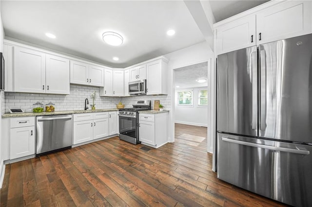 kitchen with appliances with stainless steel finishes, white cabinetry, sink, dark hardwood / wood-style floors, and light stone counters