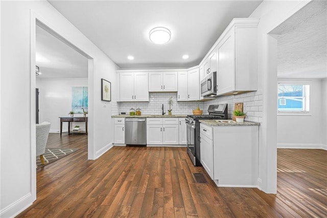 kitchen featuring decorative backsplash, white cabinets, dark hardwood / wood-style flooring, stainless steel appliances, and light stone counters