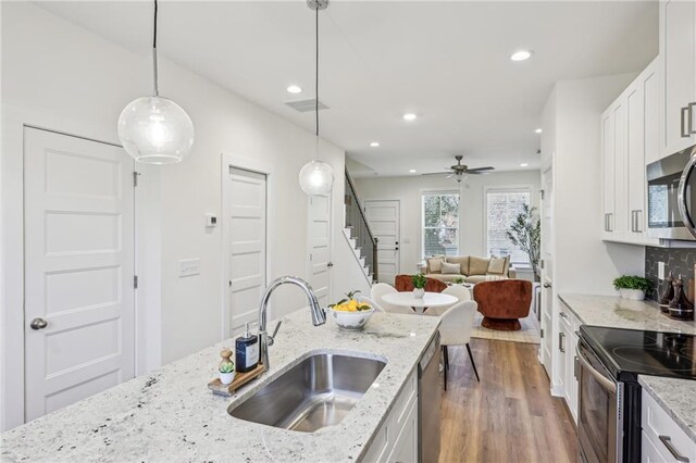 kitchen featuring sink, hanging light fixtures, stainless steel appliances, white cabinets, and light stone counters