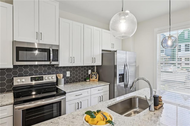 kitchen featuring light stone counters, a sink, white cabinets, appliances with stainless steel finishes, and pendant lighting