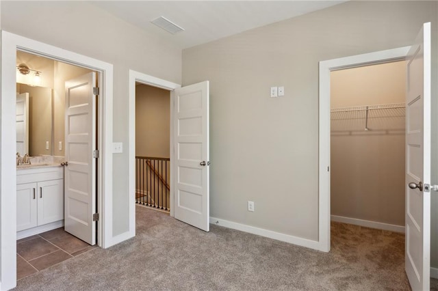 unfurnished bedroom featuring ensuite bathroom, sink, a spacious closet, light carpet, and a closet