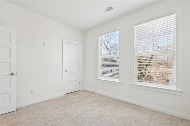 spare room featuring baseboards, a healthy amount of sunlight, visible vents, and light colored carpet