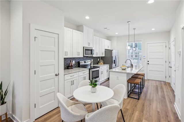 kitchen featuring appliances with stainless steel finishes, white cabinets, sink, hanging light fixtures, and a kitchen island with sink