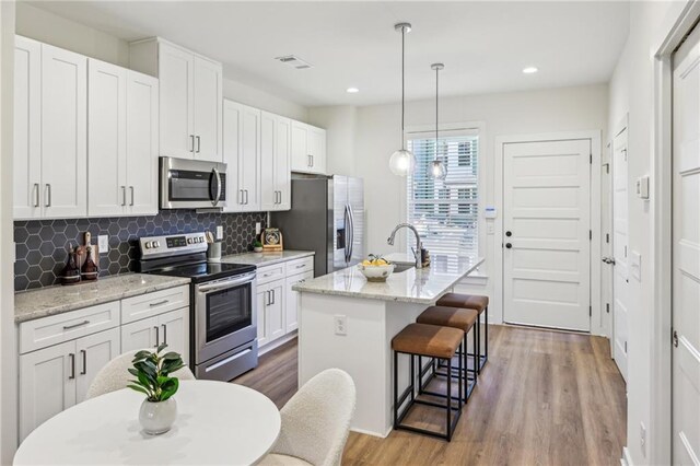 kitchen with pendant lighting, white cabinets, appliances with stainless steel finishes, sink, and a center island with sink