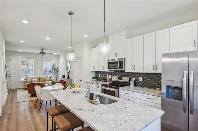 kitchen with decorative light fixtures, white cabinets, a center island with sink, and stainless steel appliances