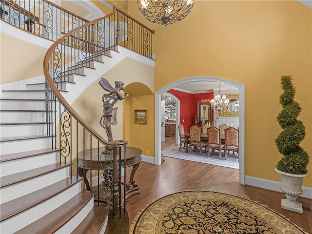 foyer entrance with a towering ceiling, an inviting chandelier, baseboards, and wood finished floors