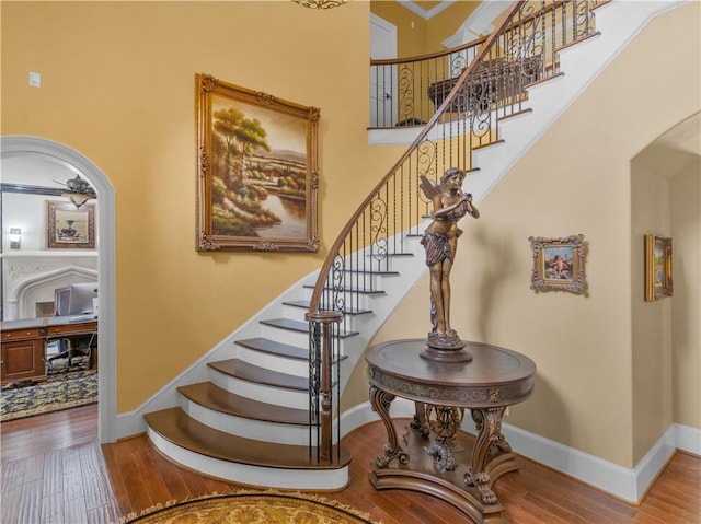 staircase featuring arched walkways, a high ceiling, baseboards, and wood-type flooring