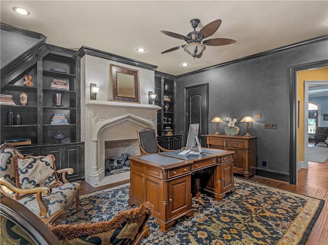 home office featuring built in shelves, wood finished floors, baseboards, a fireplace with flush hearth, and crown molding