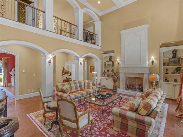 living area with a premium fireplace, baseboards, wood finished floors, and decorative columns