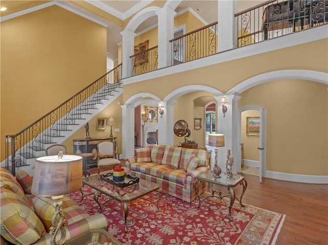 living room featuring baseboards, stairway, a high ceiling, wood finished floors, and ornate columns