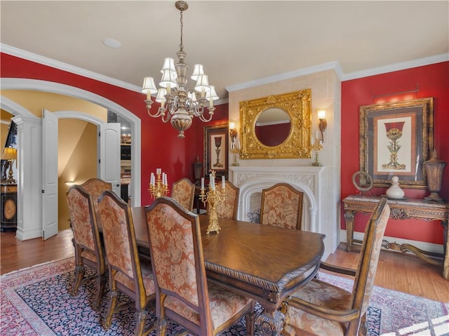 dining area with baseboards, ornamental molding, wood finished floors, arched walkways, and a notable chandelier