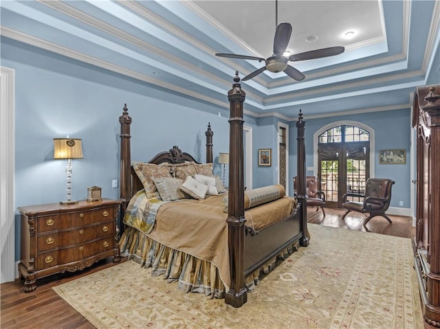 bedroom featuring ornamental molding, a tray ceiling, wood finished floors, french doors, and ceiling fan