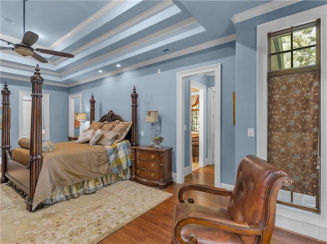 bedroom with a raised ceiling, wood finished floors, baseboards, and ornamental molding