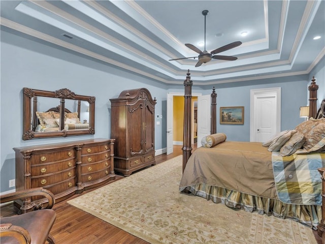 bedroom with a raised ceiling, wood finished floors, crown molding, and ceiling fan