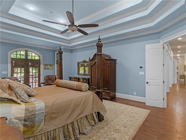 bedroom featuring baseboards, ornamental molding, french doors, wood finished floors, and a raised ceiling