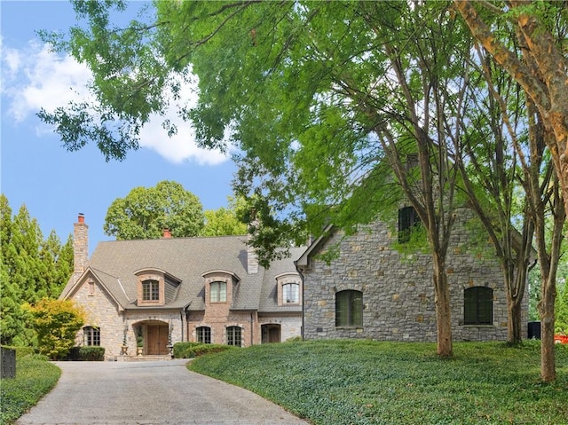 french country style house featuring driveway, a chimney, and a front lawn