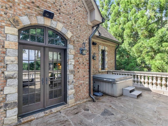 property entrance with french doors, brick siding, roof with shingles, and a hot tub