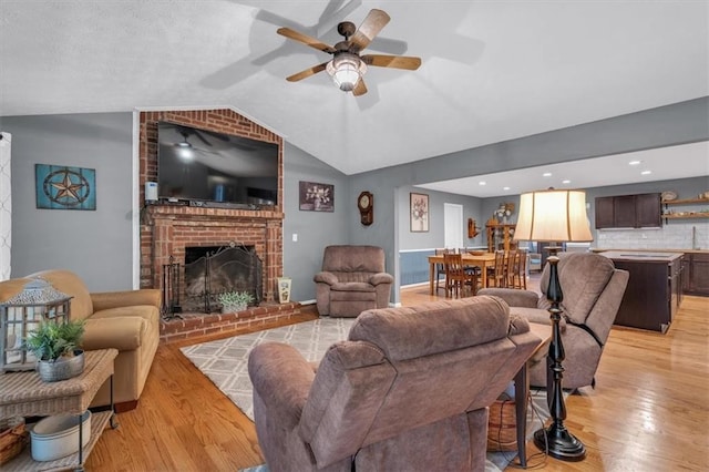 living area featuring lofted ceiling, ceiling fan, light wood-type flooring, and a fireplace