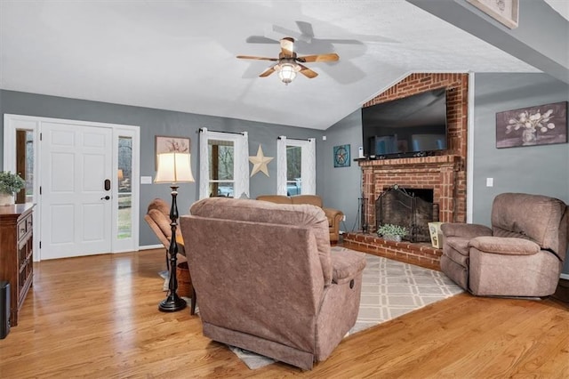 living area featuring a wealth of natural light, lofted ceiling, a brick fireplace, and light wood finished floors