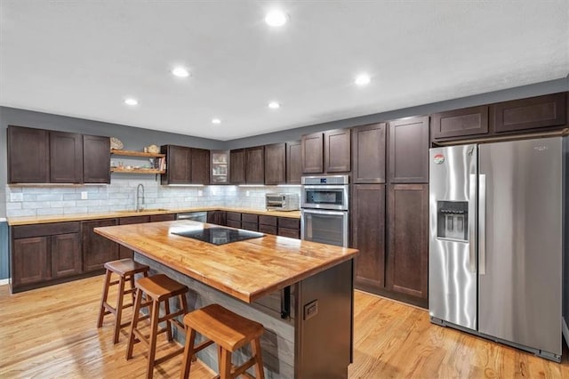 kitchen featuring a breakfast bar area, light wood finished floors, appliances with stainless steel finishes, dark brown cabinetry, and a sink