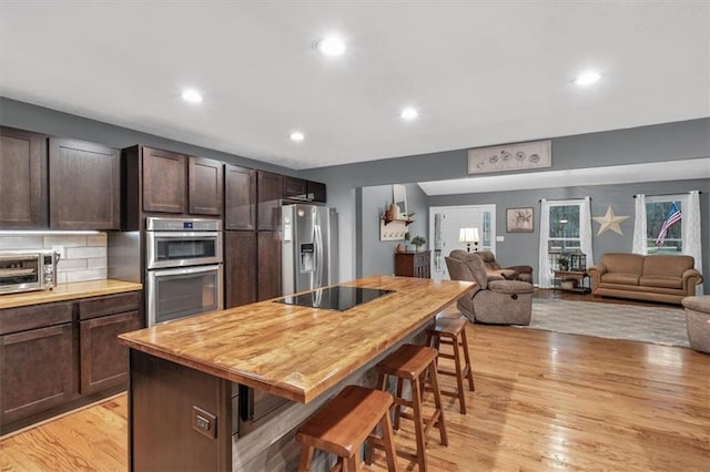 kitchen with stainless steel appliances, tasteful backsplash, light wood-style floors, dark brown cabinetry, and a kitchen breakfast bar