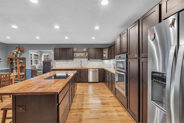 kitchen with dark brown cabinetry, stainless steel appliances, a breakfast bar, a sink, and wood counters