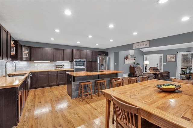 kitchen with stainless steel appliances, a sink, dark brown cabinets, light countertops, and light wood-type flooring