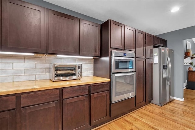 kitchen featuring a toaster, stainless steel appliances, backsplash, light wood-style floors, and dark brown cabinetry