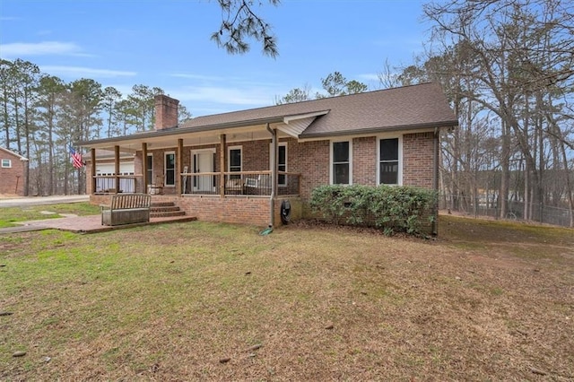 view of front of property with covered porch, brick siding, a shingled roof, a front lawn, and a chimney