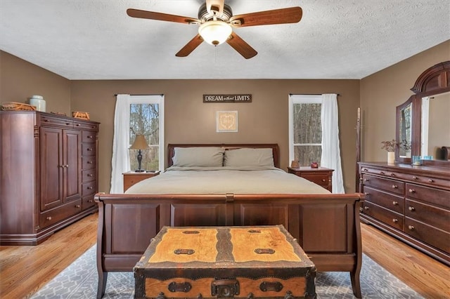 bedroom with a textured ceiling, light wood finished floors, and a ceiling fan