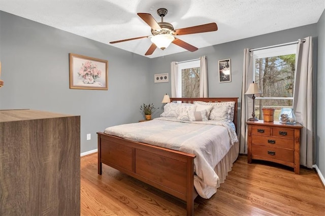 bedroom with a textured ceiling, multiple windows, baseboards, and wood finished floors