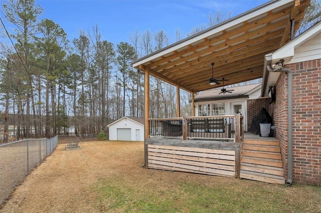 view of yard featuring driveway, ceiling fan, a detached garage, an outbuilding, and fence