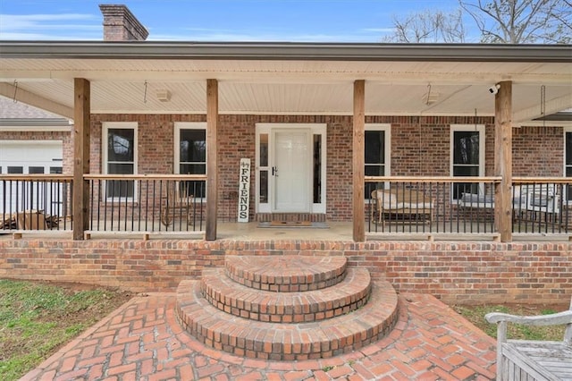 view of exterior entry with covered porch, brick siding, and a chimney