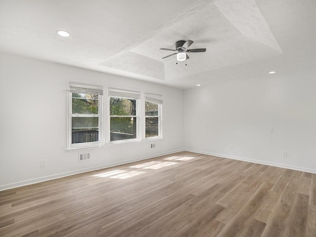 empty room featuring a ceiling fan, visible vents, light wood-type flooring, a raised ceiling, and baseboards