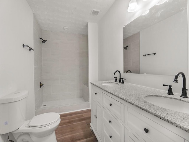 bathroom featuring a sink, toilet, tiled shower, and visible vents