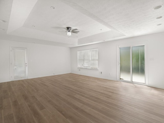 spare room featuring a textured ceiling, a ceiling fan, a tray ceiling, and wood finished floors