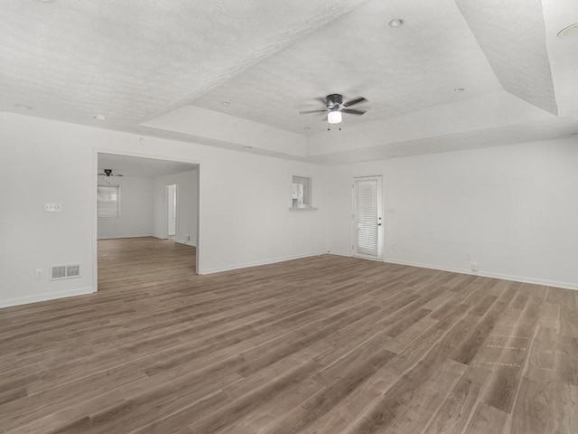 unfurnished room featuring a ceiling fan, a tray ceiling, wood finished floors, and visible vents