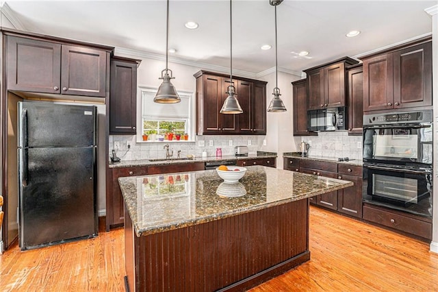 kitchen with dark brown cabinetry, dark stone counters, ornamental molding, light wood-style flooring, and black appliances