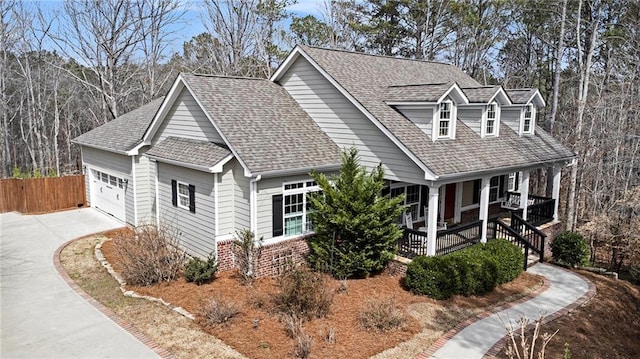 view of front facade with driveway, a porch, fence, an attached garage, and a shingled roof