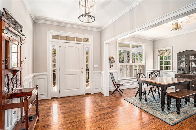 foyer entrance featuring an inviting chandelier, wood finished floors, a wainscoted wall, and ornamental molding