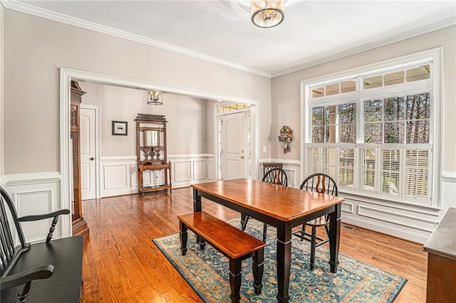 dining space featuring a wainscoted wall, wood finished floors, crown molding, and a decorative wall